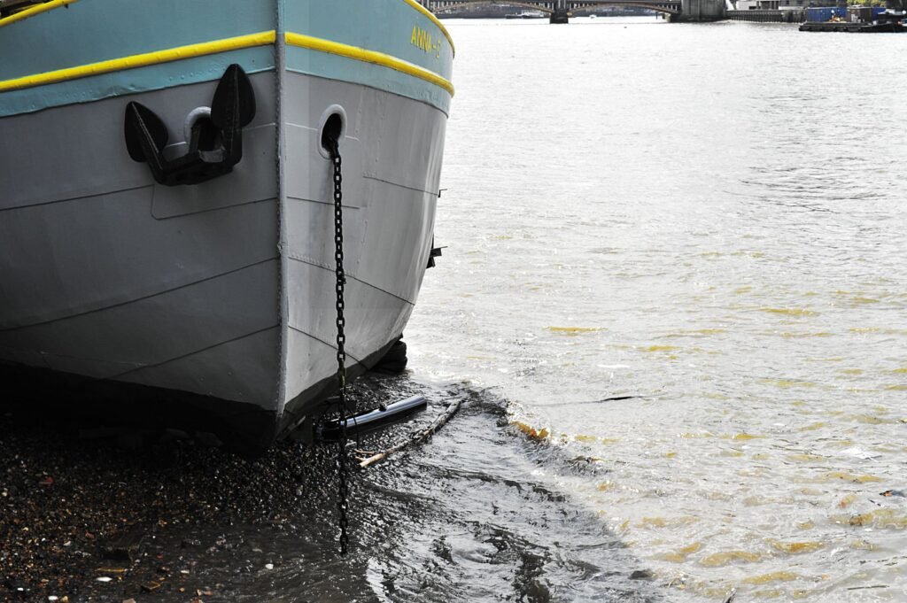 Étrave d’un bateau amarré au bord d’un fleuve, chaîne d’ancre qui descend du nez jusqu’à l’eau