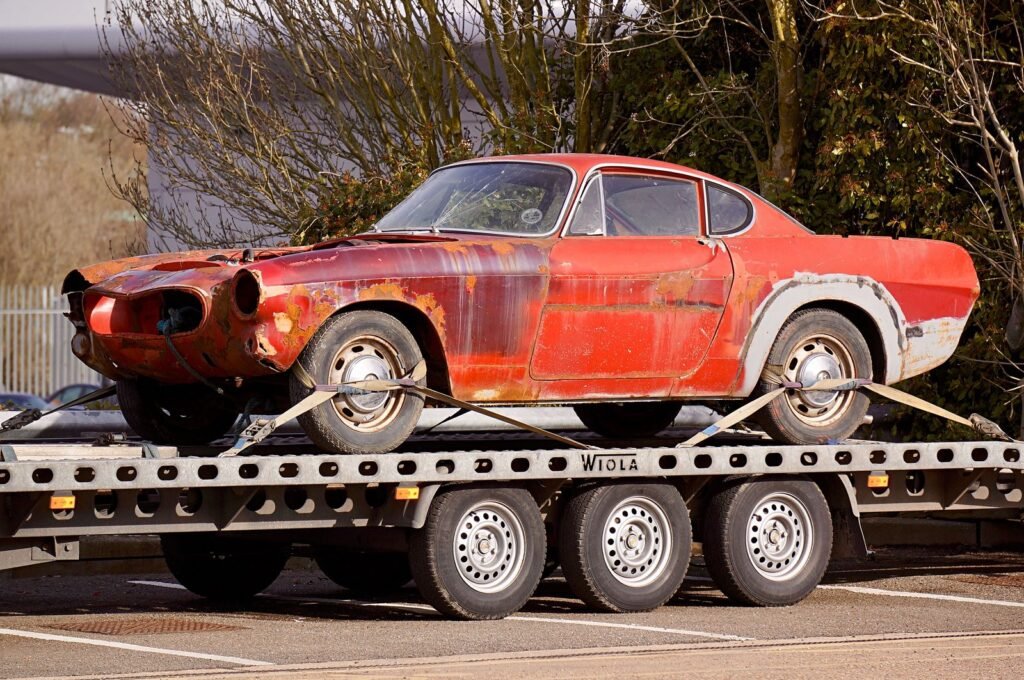 Voiture de collection rouillée sanglée par les roues sur un plateau porte-voiture